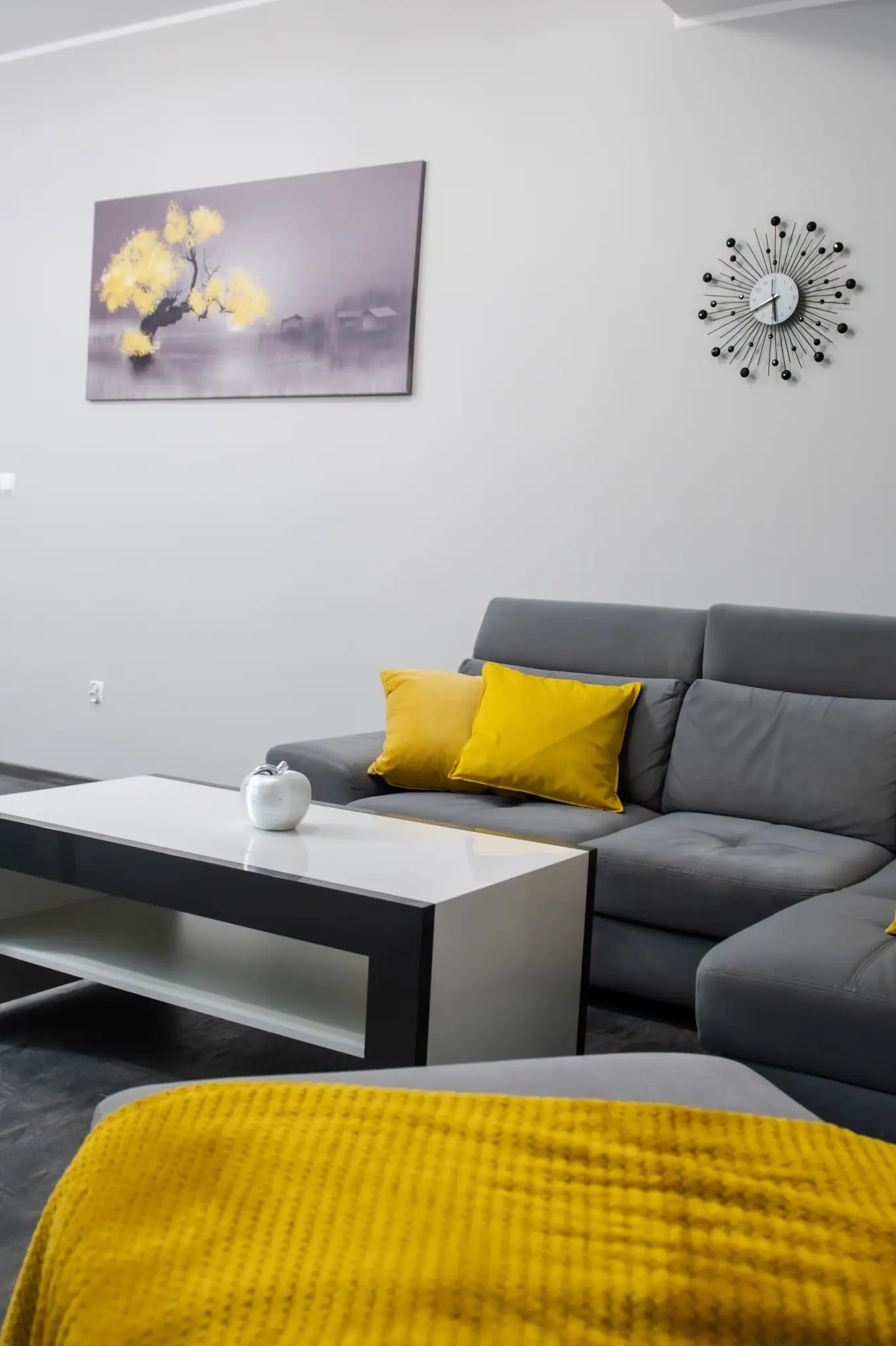Salon z szarą kanapą i żółtymi dodatkami